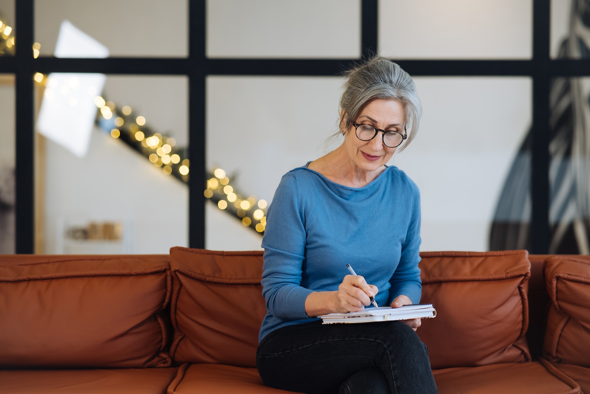 Happy senior woman in glasses writing to notebook at home